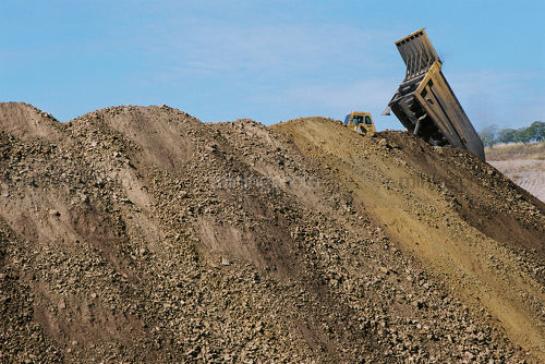 Haul truck emptying load of overburden next to many mounds of stockpiles. - Mining Photo Stock Library