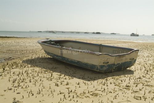 Row boat on the sand flats at low tide with boats in the background on the ocean. - Mining Photo Stock Library
