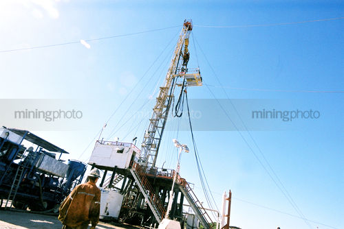 Drill rig worker in full PPE walking towards derrick on site.  shot from behind - Mining Photo Stock Library