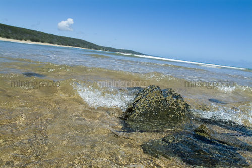 Clean beach with ocean surf water breaking over rocks. shot from water level  - Mining Photo Stock Library