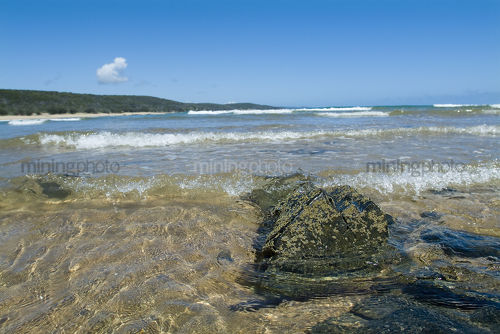 Clean beach with ocean surf water breaking over rocks. shot from water level  - Mining Photo Stock Library