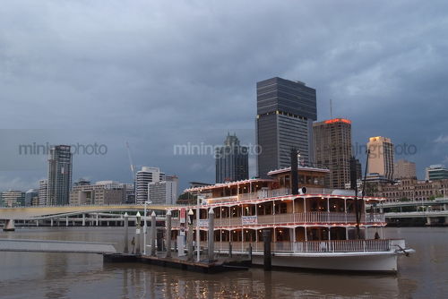 Brisbane building skyline after a storm with paddle steamer boat on the river in foreground at wharf - Mining Photo Stock Library