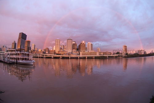 Sunset rainbow brisbane building skyline after a storm with paddle steamer boat on the river in foreground at wharf - Mining Photo Stock Library