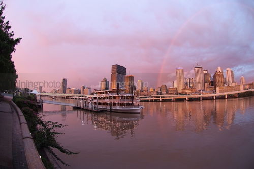 Brisbane city skyline after storm with rainbow at sunset.  paddle steamer boat in foreground on the river. - Mining Photo Stock Library