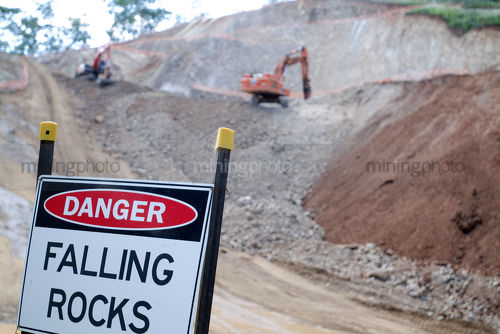 Two excavators working at tiered quarry blasting site.  danger falling rocks sign in foreground. - Mining Photo Stock Library