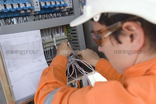 Female mine site electrical engineer in full PPE looking at plans and wiring up machinery.  shot from the side and behind. - Mining Photo Stock Library