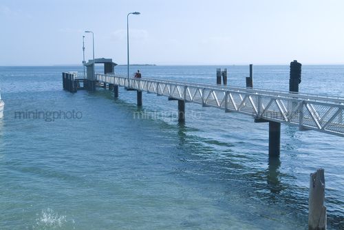 Person walking along pedestrian jetty above ocean. - Mining Photo Stock Library