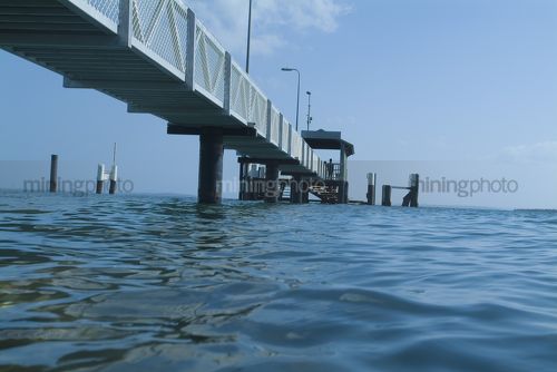 Person standing at the end of pedestrian jetty waiting for ferry.  shot from water level. - Mining Photo Stock Library