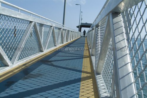 Person silhouetted at the end of a pedestrian jetty.  shot from ground level looking along the jetty. - Mining Photo Stock Library