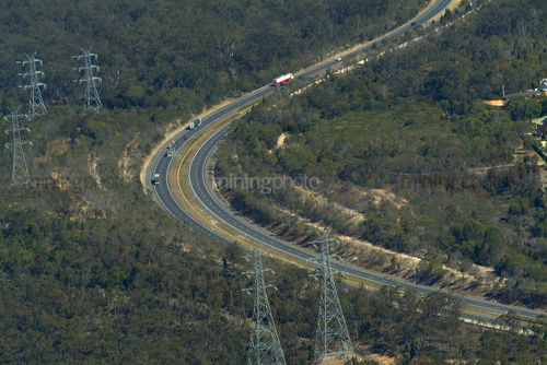 Trucks on highway through forest with electricity supply power lines adjacent.  aerial shot. - Mining Photo Stock Library
