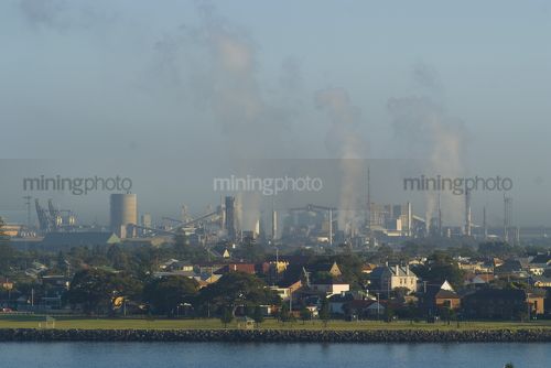 Pollution and heavy industry in background with city and residential in front and river in foreground. carbon emission offset image. - Mining Photo Stock Library