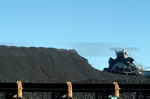 Reclaimer working amongst stockpiled coal with conveyor in foreground - Mining Photo Stock Library