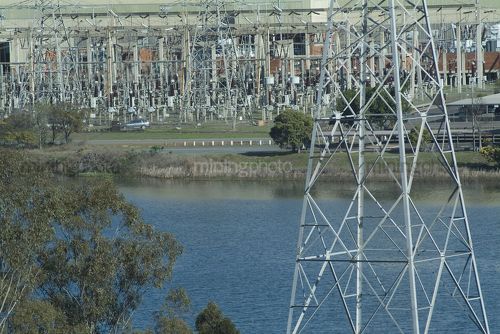 Electricity tower and substation in background with lake in foreground.  - Mining Photo Stock Library