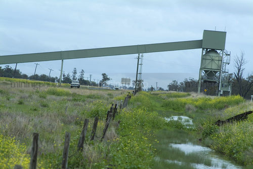 Covered coal conveyor over rural highway into hopper for rail transport. - Mining Photo Stock Library