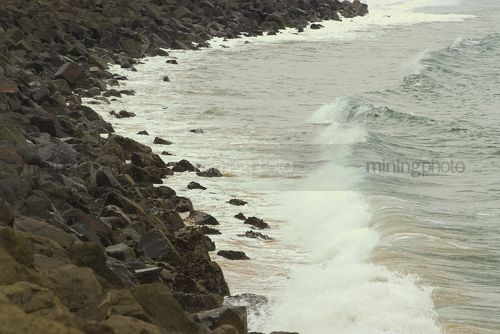Waves from the ocean washing against rock retaining wall - Mining Photo Stock Library