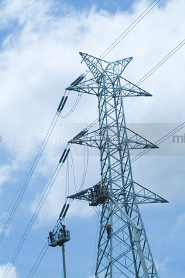 Electricity maintenance workers high up on a tower. - Mining Photo Stock Library