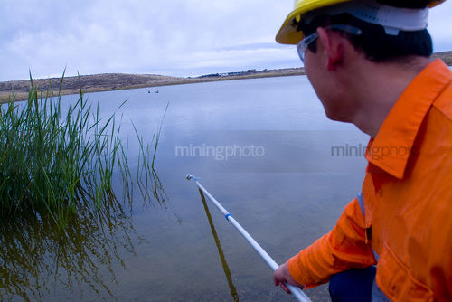 Mine environment worker taking water samples from dam at open  cut mine.  shot from behind - Mining Photo Stock Library