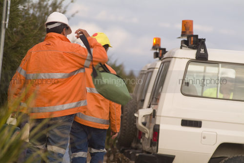 Worker slinging his bag over shoulder walking to crew vehicle. shot from behind. - Mining Photo Stock Library