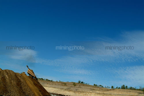 Haul truck tipping overburden onto huge stockpile. small in frame with lots of blue sky for text. - Mining Photo Stock Library