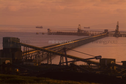 Long wharf out to ships being loaded at sunset. - Mining Photo Stock Library