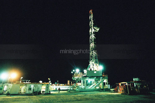 Desert oil rig shot at nigth under lights with a single worker in the shot for scale. - Mining Photo Stock Library