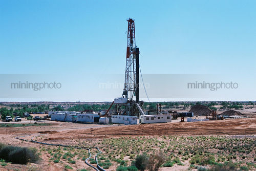 Desert oil and gas rig during the day shot from afar to give scope of remote location. - Mining Photo Stock Library