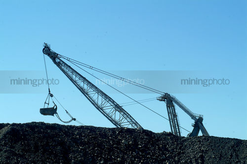 Silhouette of drag line excavator behind stockpiled coal - Mining Photo Stock Library