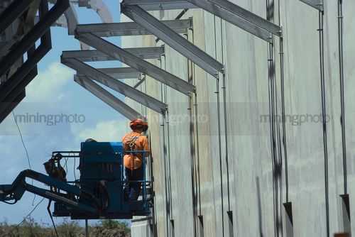 Worker in a cherry picker up high next to pre-cast concrete form work. - Mining Photo Stock Library