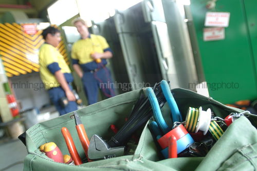 Maintenance worker's tool belt with workers out of focus in background. - Mining Photo Stock Library