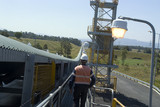 Mining Photo Stock Library - worker in PPE walking on walkway adjacent to covered coal conveyor. conveyor disappears into the distance, shot from behind. ( Weight: 4  New Image: NO)