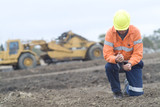 Mining Photo Stock Library - mine worker on haunches sifting soil overburden through hands with scraper machinery in background. great generic mine shot with room for text. ( Weight: 1  New Image: NO)