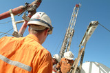Mining Photo Stock Library - oil and gas rig workers working together on a rig with the derrick in the background. shot from behind. ( Weight: 3  New Image: NO)