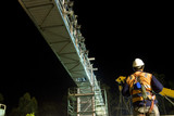 Mining Photo Stock Library - rigger worker in full PPE including a harness working under a bridge at night.  crane and scaffolding in the background.  shot from behind. ( Weight: 1  New Image: NO)