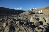 Mining Photo Stock Library - vertical photo of digger excavator loading a 789 haul truck in open cut mine site.  photo shot from ground level.  truck in distance driving along ridge top as scale. ( Weight: 1  New Image: NO)
